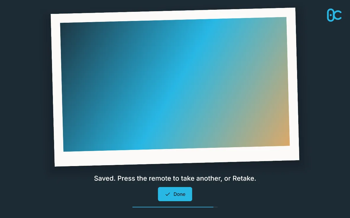 The result screen: the photo as a tilted print with the logo, “Saved. Press the remote to take another, or Retake.” and Done, on a large screen in landscape.