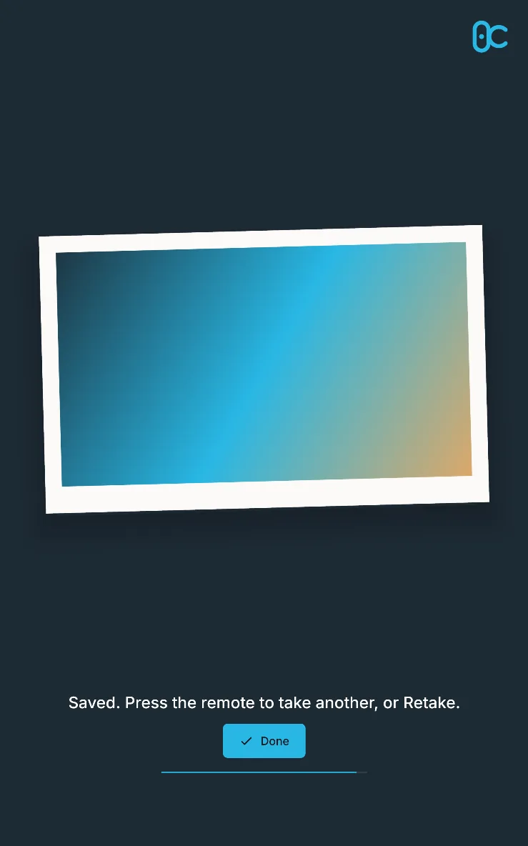 The result screen: the photo as a tilted print with the logo, “Saved. Press the remote to take another, or Retake.” and Done, on a large screen in portrait.